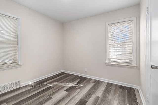 unfurnished room with dark wood-style floors, visible vents, and baseboards