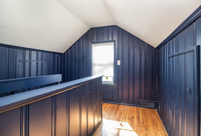 additional living space with visible vents, vaulted ceiling, wood walls, and light wood finished floors