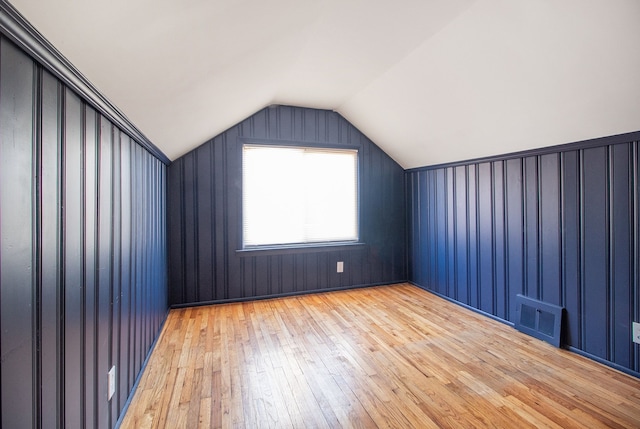 additional living space featuring light wood-style floors, visible vents, and vaulted ceiling