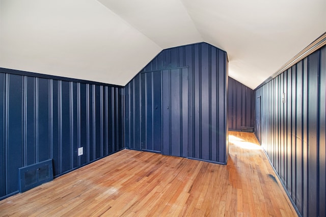 additional living space with light wood finished floors, visible vents, and vaulted ceiling