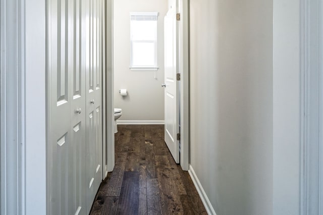 corridor featuring dark wood-type flooring and baseboards