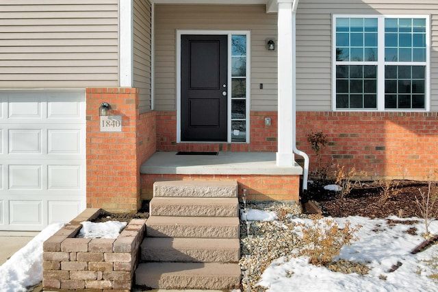 snow covered property entrance featuring a garage and brick siding