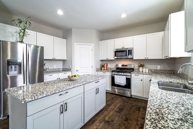 kitchen featuring white cabinets, appliances with stainless steel finishes, dark wood-type flooring, a center island, and a sink