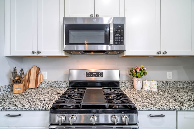 kitchen with stainless steel appliances, white cabinetry, and dark stone countertops