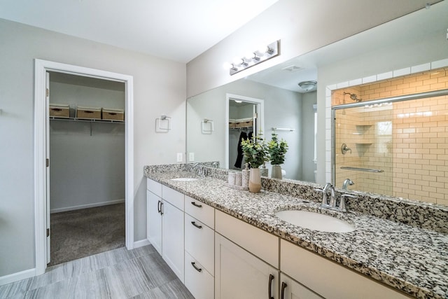 bathroom with double vanity, a shower stall, a walk in closet, and a sink