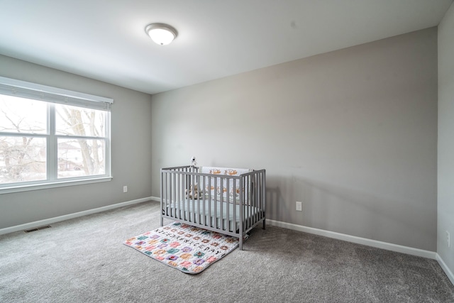 carpeted bedroom featuring a crib, baseboards, and visible vents