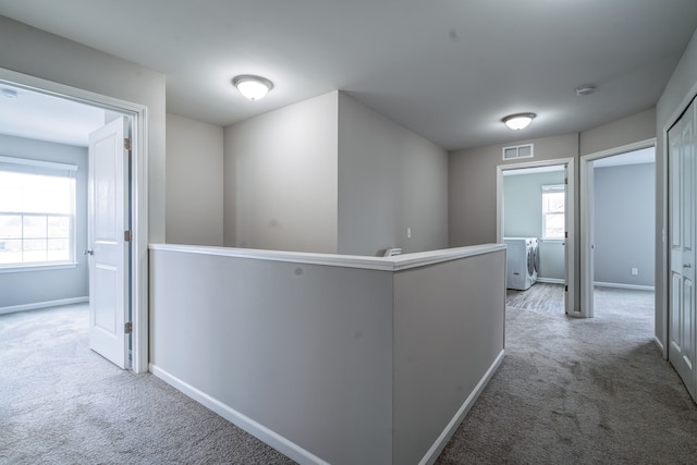 hallway featuring carpet flooring, an upstairs landing, visible vents, baseboards, and independent washer and dryer