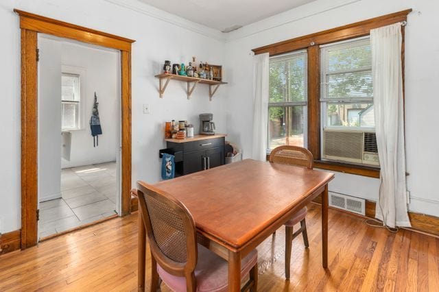 dining room with light wood-type flooring, visible vents, and ornamental molding