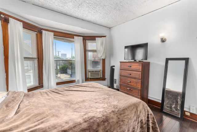 bedroom with dark wood-style floors, a textured ceiling, cooling unit, and baseboards