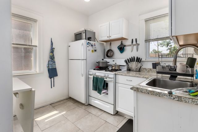 kitchen featuring light tile patterned floors, white cabinets, a sink, light stone countertops, and white appliances