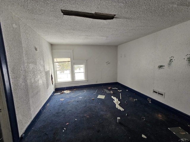 empty room featuring a textured ceiling, visible vents, and baseboards