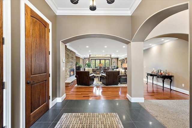 entryway featuring dark tile patterned floors, ornamental molding, baseboards, and a stone fireplace