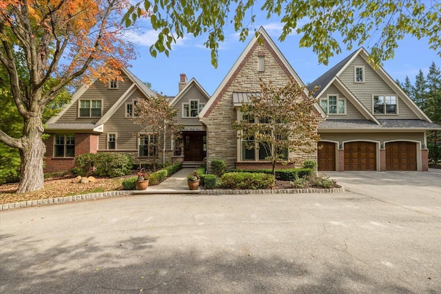 view of front of property with a chimney, driveway, stone siding, an attached garage, and brick siding