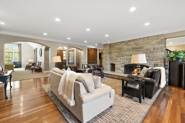 living room with arched walkways, a stone fireplace, light wood finished floors, and ornamental molding