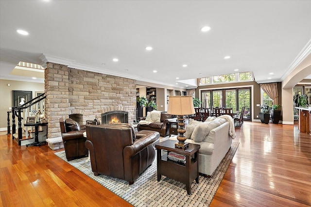 living area with recessed lighting, a stone fireplace, crown molding, and light wood-style flooring