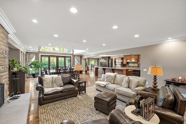 living area with recessed lighting, a stone fireplace, crown molding, and light wood-style flooring