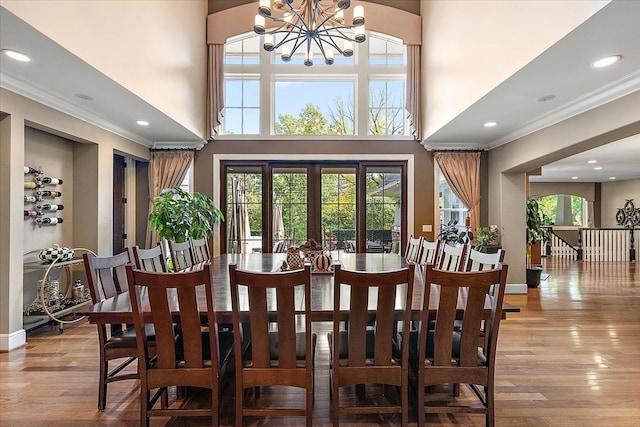 dining space featuring a towering ceiling, light wood-style floors, plenty of natural light, and ornamental molding