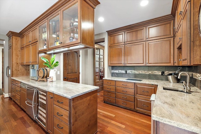 kitchen with glass insert cabinets, brown cabinetry, a sink, and light stone counters