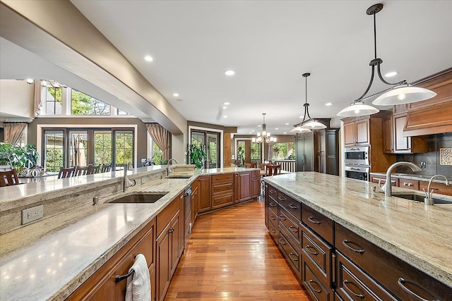 kitchen featuring light wood-type flooring, light stone counters, a sink, and decorative light fixtures