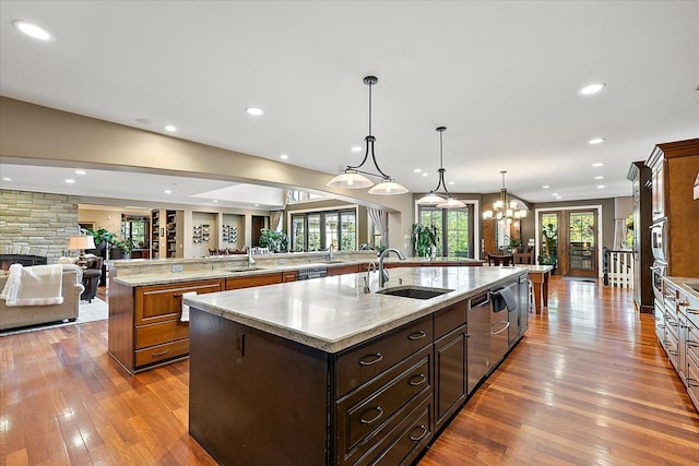 kitchen featuring open floor plan, hanging light fixtures, a large island with sink, a stone fireplace, and a sink