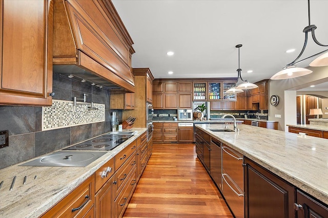 kitchen with glass insert cabinets, brown cabinets, light stone counters, custom exhaust hood, and pendant lighting