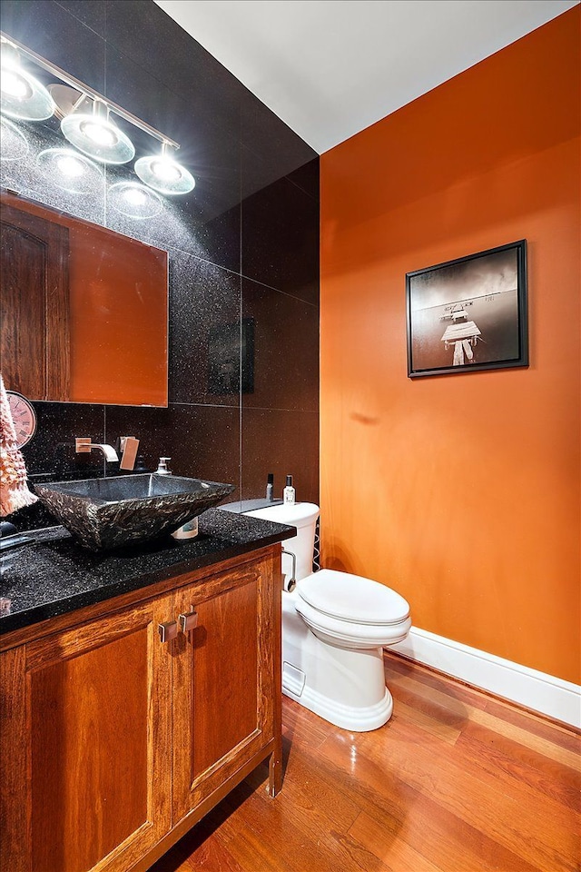 half bath featuring baseboards, toilet, wood finished floors, vanity, and tile walls