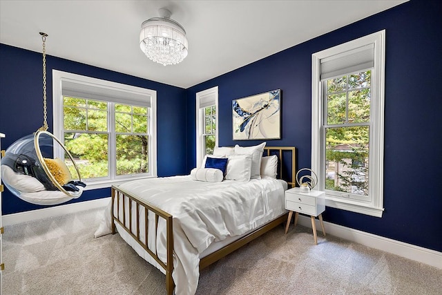 carpeted bedroom featuring multiple windows, a notable chandelier, and baseboards