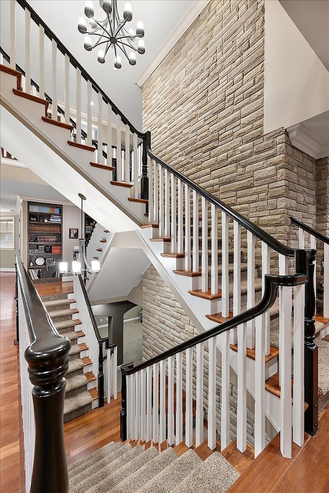 stairway featuring a towering ceiling, crown molding, a chandelier, and wood finished floors