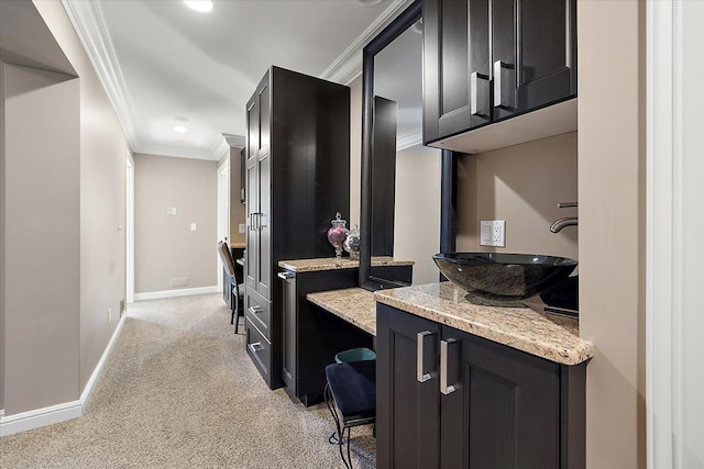 interior space with light colored carpet, dark cabinets, a sink, ornamental molding, and light stone countertops