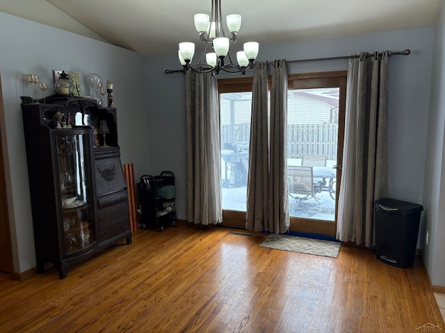 unfurnished dining area with lofted ceiling, wood finished floors, and an inviting chandelier