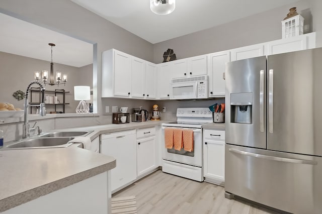 kitchen featuring light wood finished floors, light countertops, white cabinetry, a sink, and white appliances