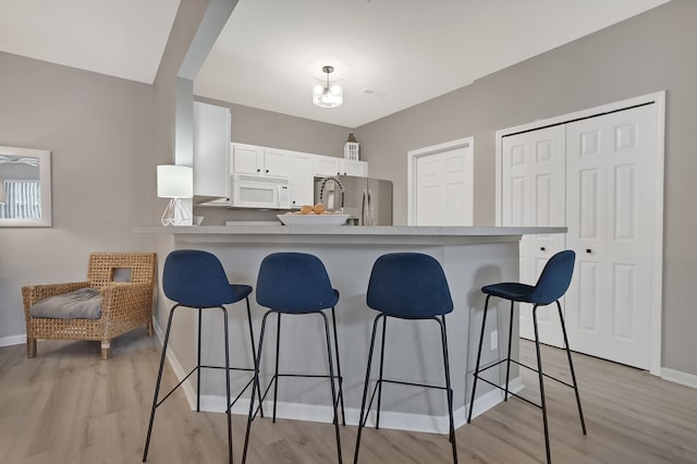 kitchen featuring white cabinets, white microwave, a kitchen breakfast bar, and freestanding refrigerator