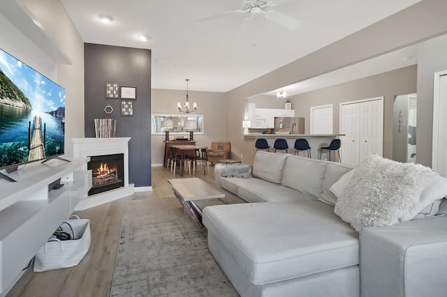 living area featuring a lit fireplace, wood finished floors, and ceiling fan with notable chandelier