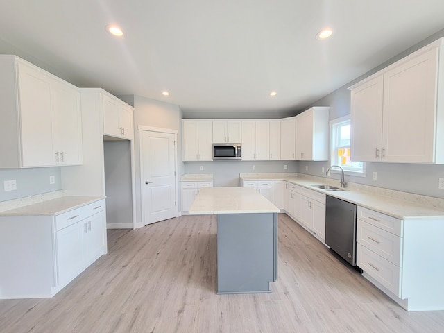 kitchen with a kitchen island, appliances with stainless steel finishes, light countertops, white cabinetry, and a sink