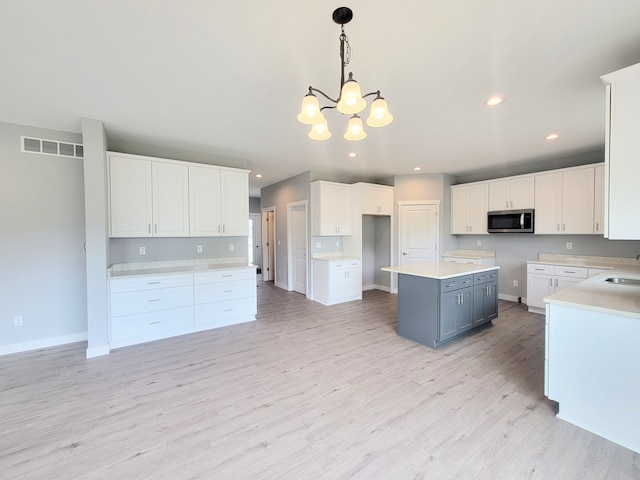 kitchen with a kitchen island, stainless steel microwave, hanging light fixtures, light countertops, and white cabinetry