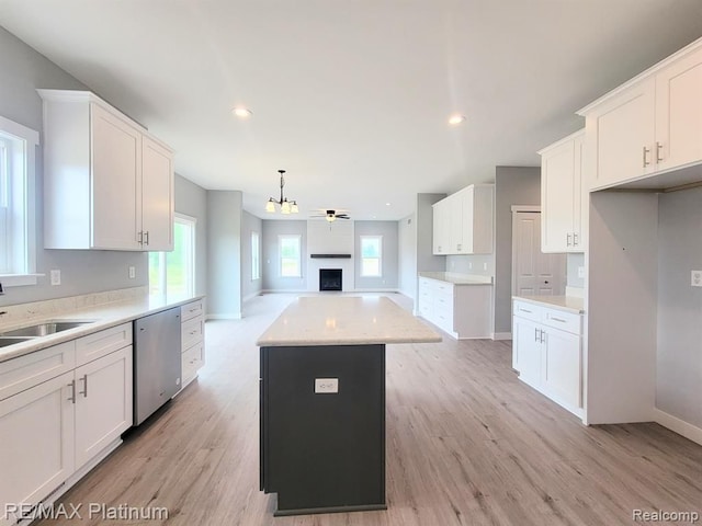 kitchen featuring a sink, white cabinetry, light countertops, stainless steel dishwasher, and a center island