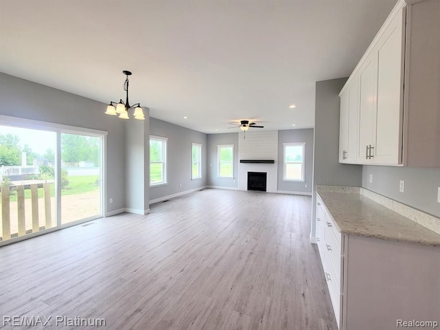 unfurnished living room featuring recessed lighting, light wood-style floors, a large fireplace, baseboards, and ceiling fan with notable chandelier