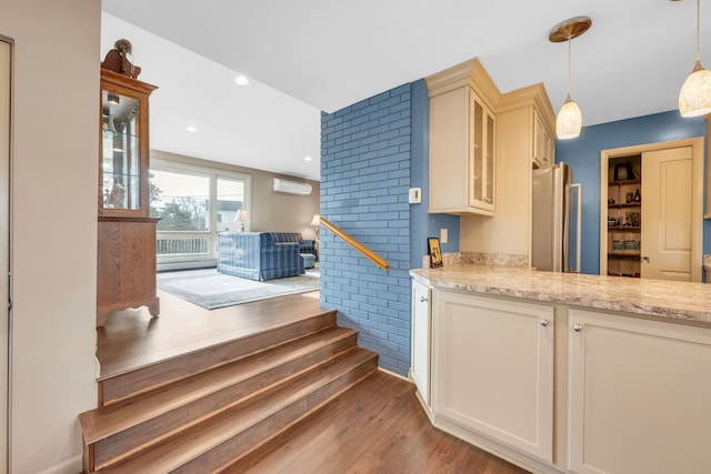 kitchen with glass insert cabinets, dark wood-style flooring, freestanding refrigerator, hanging light fixtures, and cream cabinetry