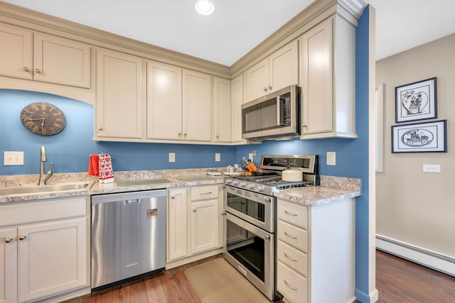 kitchen featuring dark wood-style floors, stainless steel appliances, cream cabinets, baseboard heating, and a sink