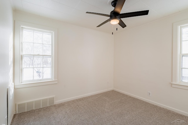 carpeted empty room featuring crown molding, a ceiling fan, visible vents, and baseboards