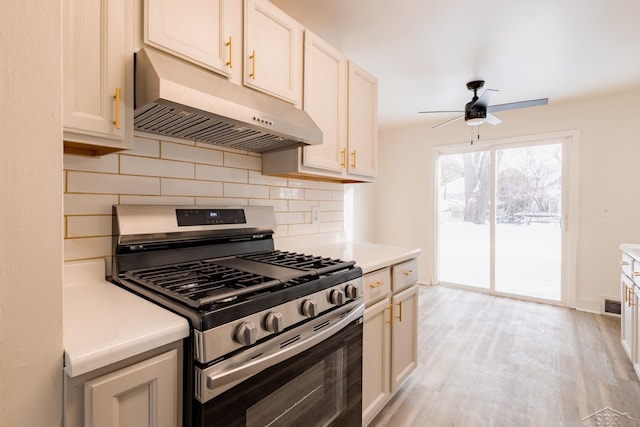 kitchen featuring backsplash, light countertops, under cabinet range hood, and stainless steel gas range oven