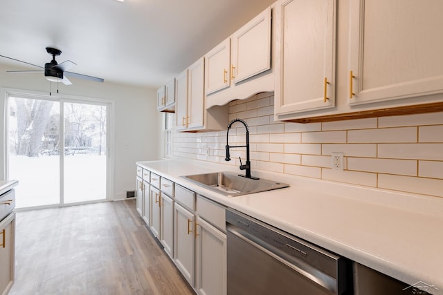 kitchen featuring light countertops, decorative backsplash, stainless steel dishwasher, a sink, and light wood-type flooring