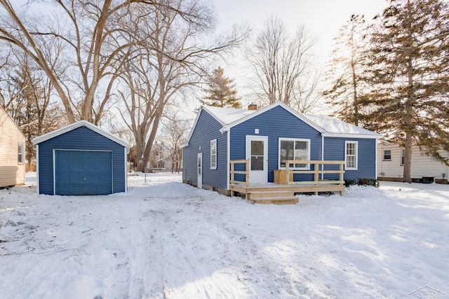 snow covered rear of property featuring a garage, a chimney, and an outdoor structure