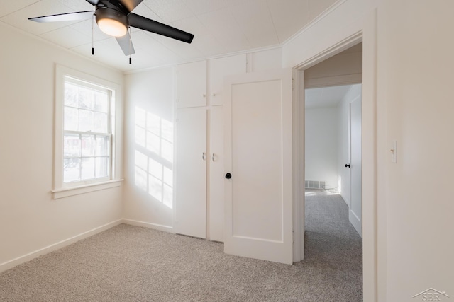 empty room featuring carpet, visible vents, ornamental molding, and ceiling fan