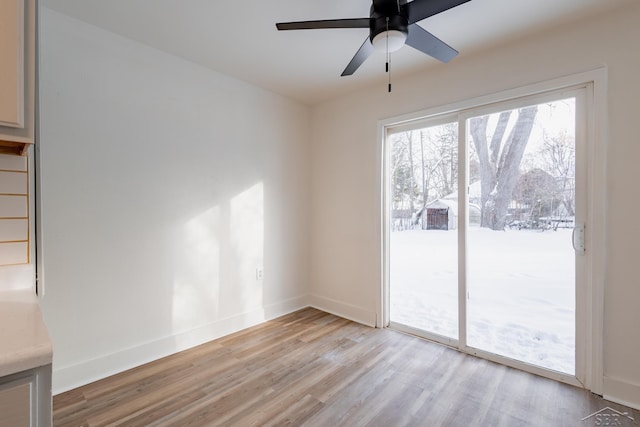 spare room featuring light wood-type flooring, a ceiling fan, and baseboards