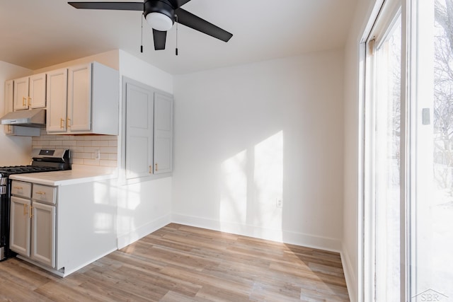 kitchen with stainless steel gas stove, light wood-style floors, light countertops, under cabinet range hood, and backsplash