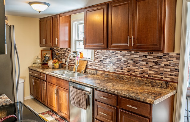 kitchen featuring a sink, appliances with stainless steel finishes, tasteful backsplash, brown cabinetry, and dark stone countertops