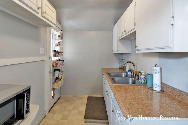 kitchen with light floors, light countertops, stainless steel microwave, white cabinets, and a sink