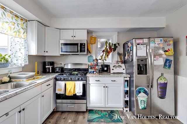 kitchen featuring appliances with stainless steel finishes, light wood-type flooring, a wealth of natural light, and white cabinets