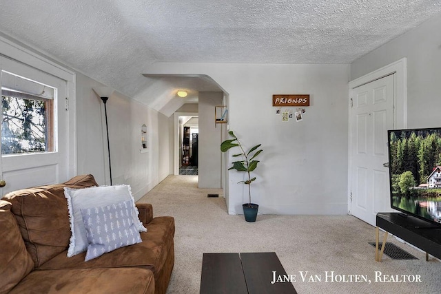 living area featuring light carpet, visible vents, arched walkways, and a textured ceiling